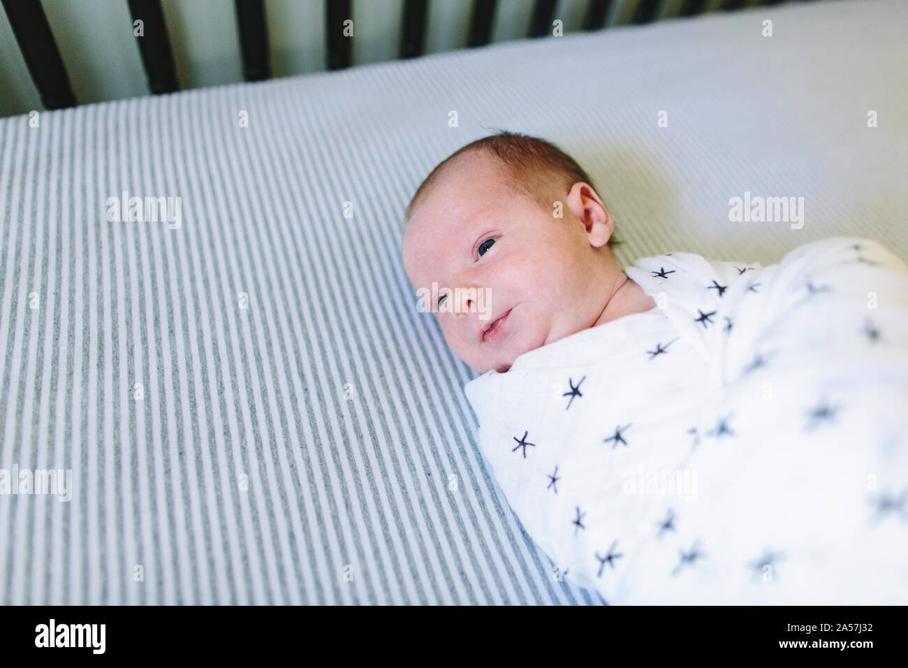 A newborn baby laying in his crib while swaddled Stock Photo