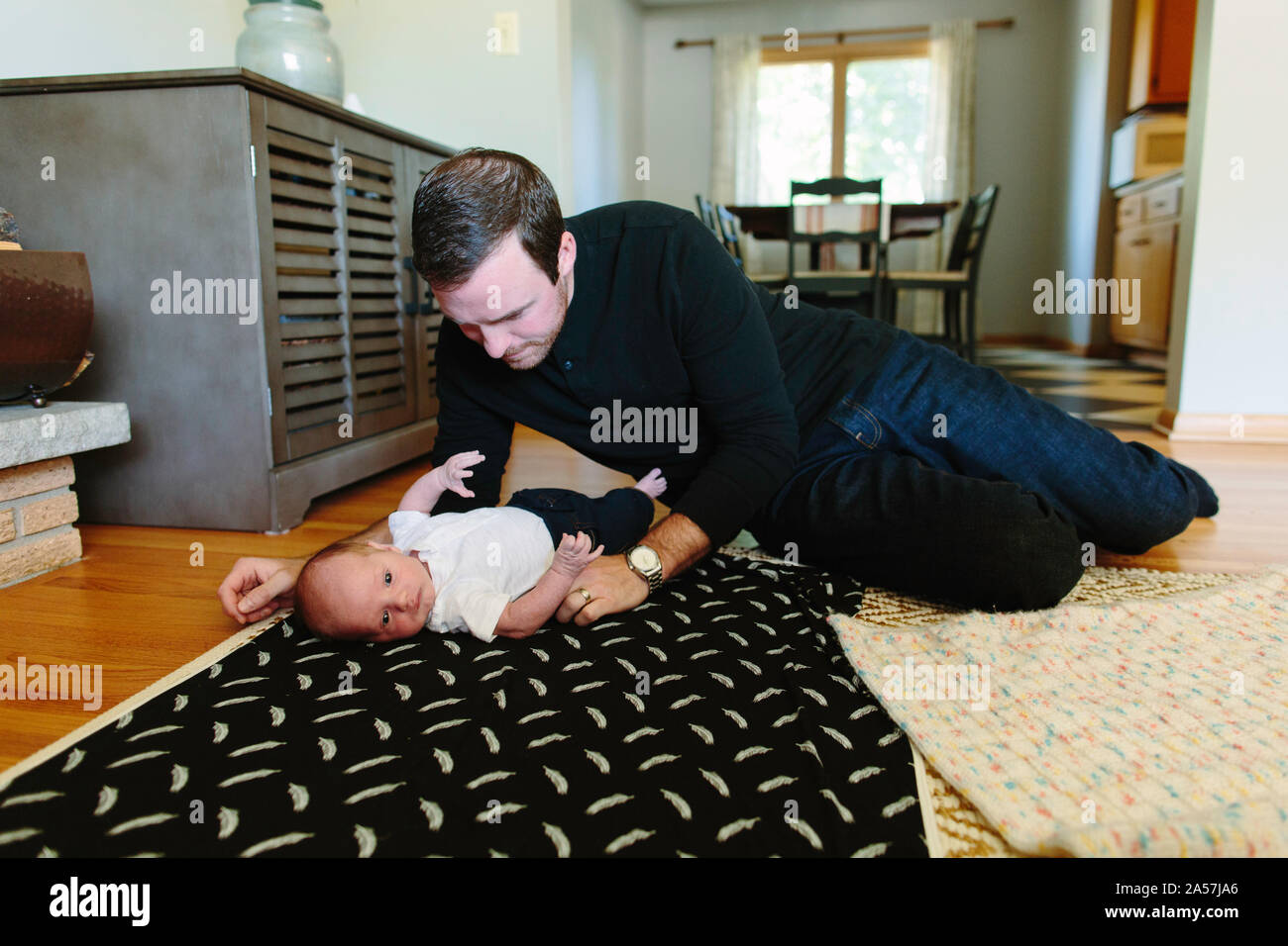A first time dad lays on the floor with his newborn baby son Stock