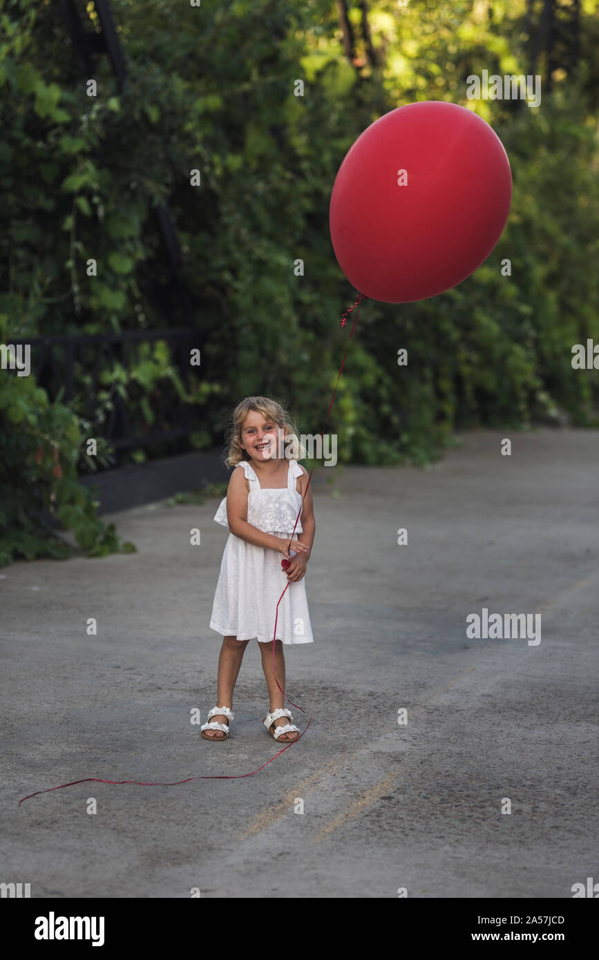 Happy young girl in white sundress holding huge red balloon Stock Photo