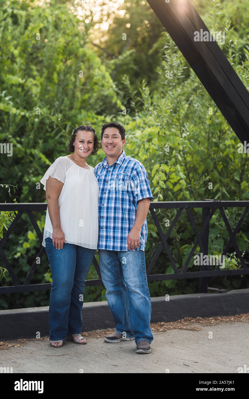 Joyful couple snuggled close on bridge in front of lush foliage Stock Photo