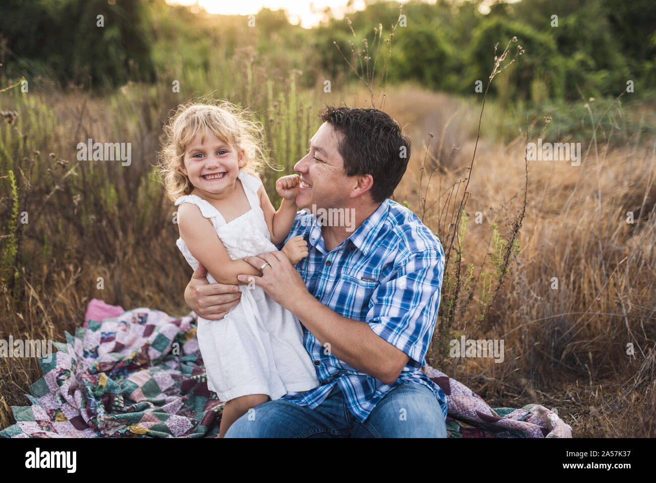 Laughing dad and young daughter on patchwork quilt in a meadow Stock Photo