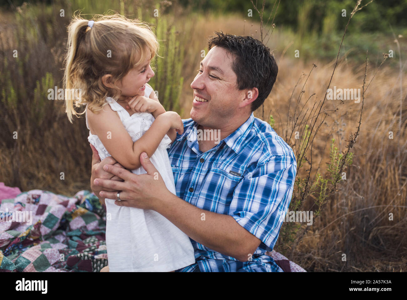 Dad and young daughter laughing together outdoors on a quilt Stock Photo