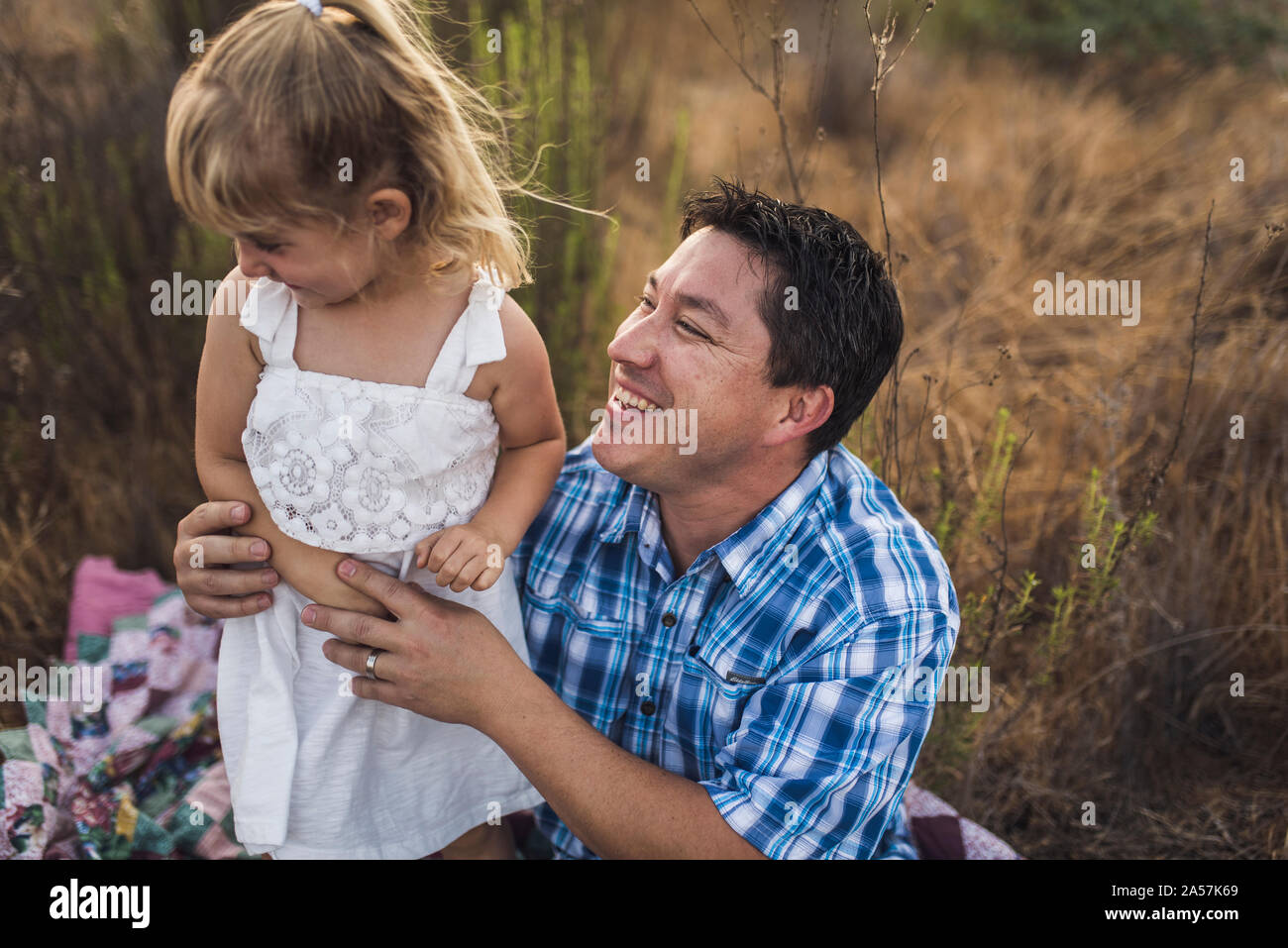 Dad smiling at 4 yr old daughter in sundress on quilt - B/W photo Stock Photo