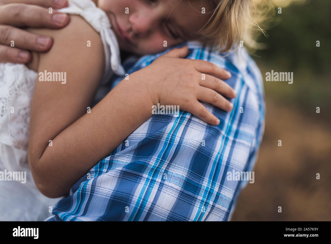 Sleeping child snuggles on her dad's shoulder in a sunny meadow Stock Photo