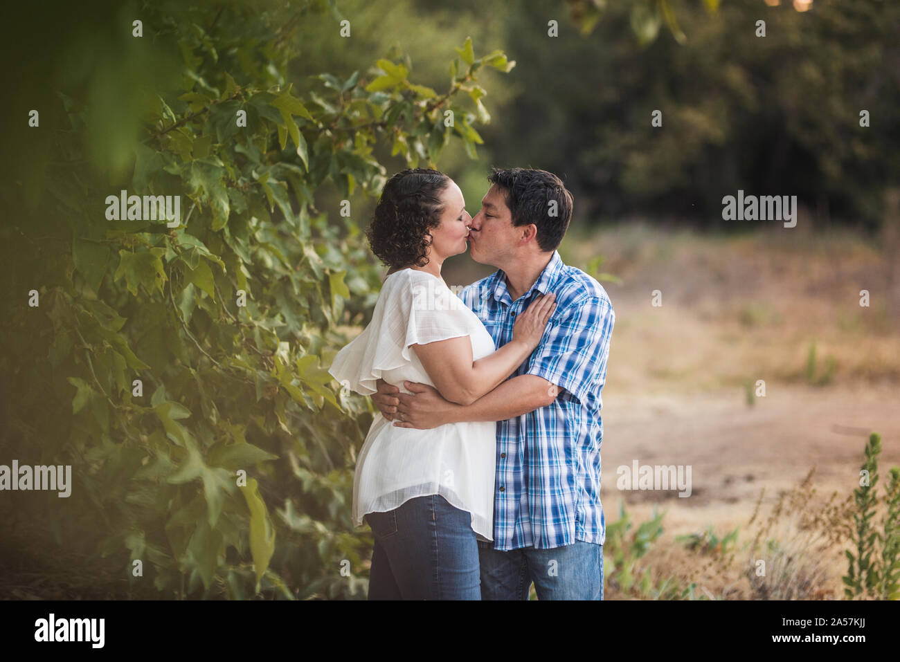 Husband and wife kissing near lush foliage Stock Photo