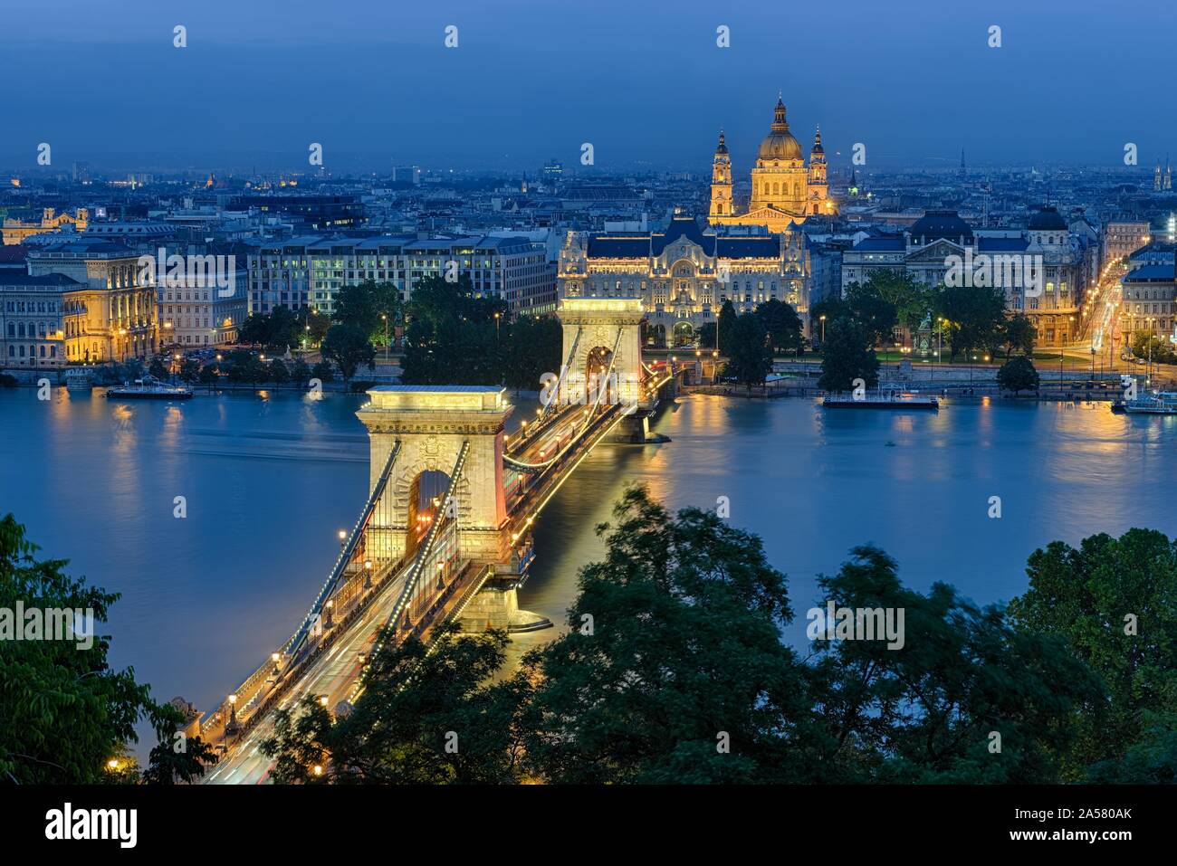 Chain bridge with Gresham Palace and St. Stephen's Basilica, illuminated, dusk, Budapest, Hungary Stock Photo