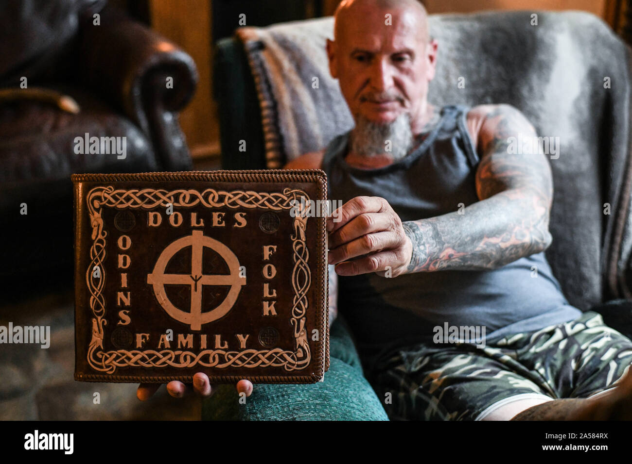 Dahlonega, Georgia, USA. 17th Sep, 2019. Doles sits in his living room, and displays a book he treasures, The Holy Book of the Aryan Tribes by Ron McVan, which is wrapped in a leather cover Doles carved with the title, 'Doles Family Odins Folk. Credit: Miguel Juarez Lugo/ZUMA Wire/Alamy Live News Stock Photo