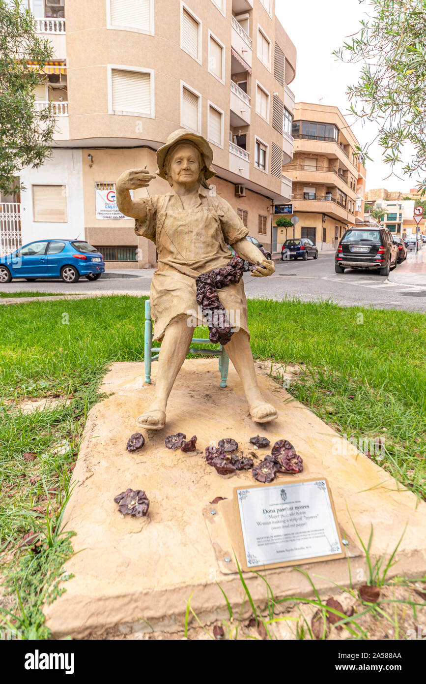 Dona Passant Nyores in Guardamar del Segura, Spain, Europe. Resin and sand sculpture of woman making a strip of sweet dried red pepper. Agriculture Stock Photo