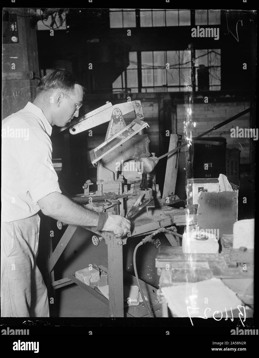 Uncle Sam makes own glass. Washington, D.C. Aug. 24. All optical glass used by the United States Navy is manufactured and finished by the Bureau of Standards in Washington. L. Maxwell, of the Glass Section, Bureau of Standards, is shown cutting molten glass into the mold. He uses ordinary tailor's shears in cutting the hot substance which is about as soft as hot molasses candy Stock Photo