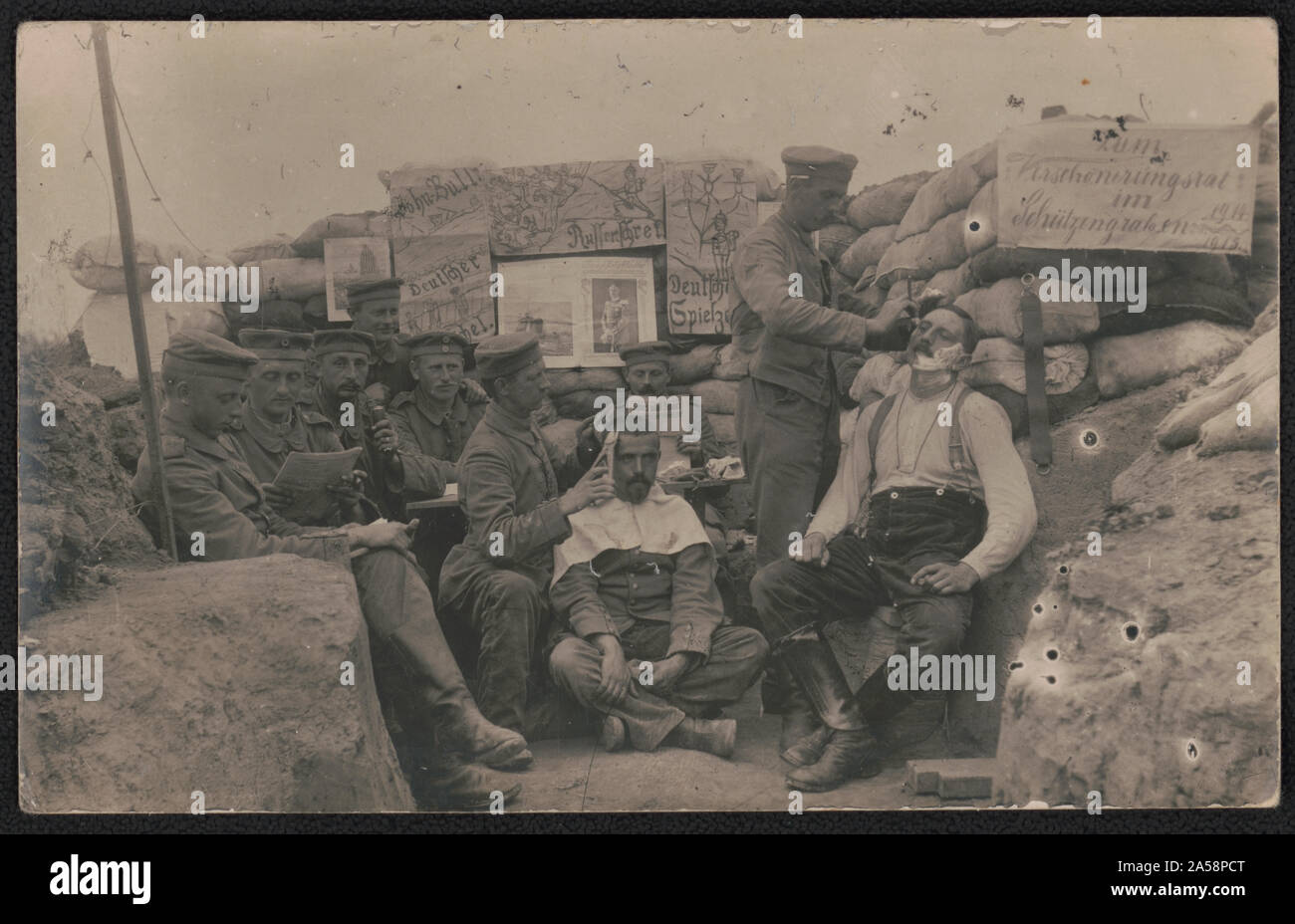 Unidentified German soldiers, some in uniform, seated in trench reading as two get a haircut and shave Stock Photo