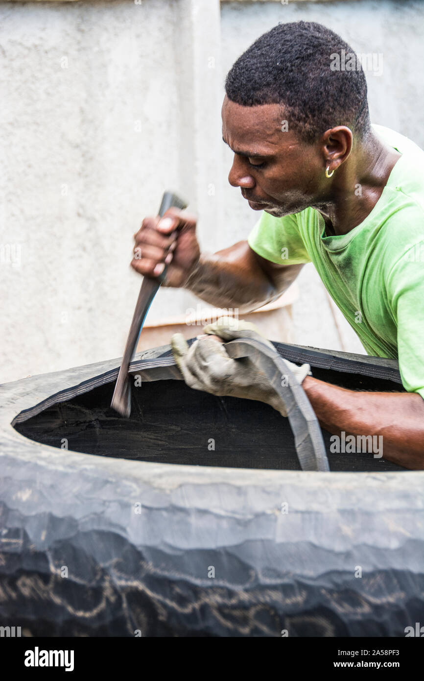 A man using a tool to cut rubber from tires that he then uses to sell