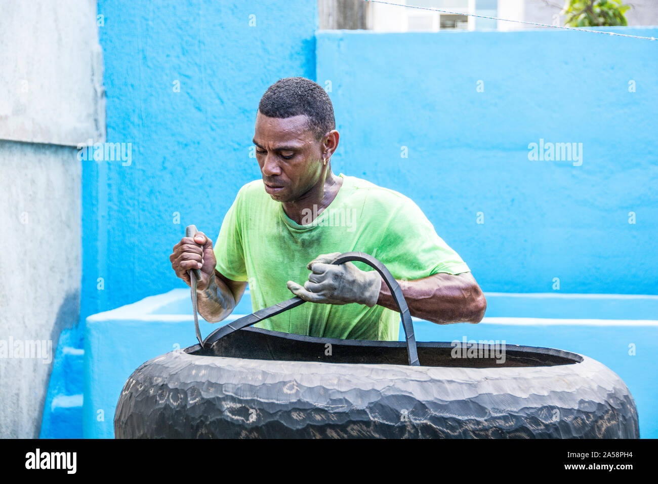 A man using a tool to cut rubber from tires that he then uses to sell