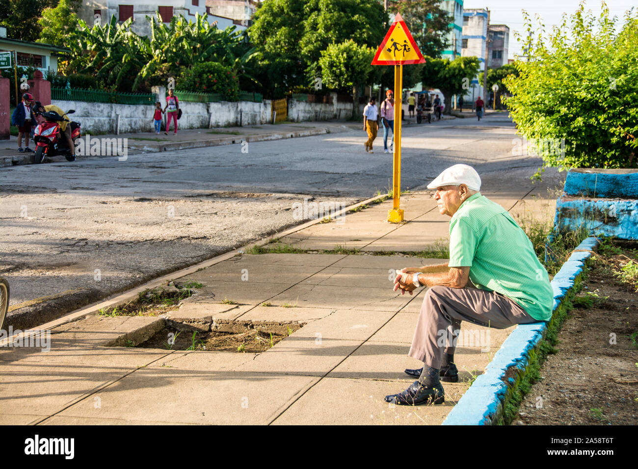 An old Cuban man sitting on the side of a sidewalk; Camaguey, Cuba Stock Photo