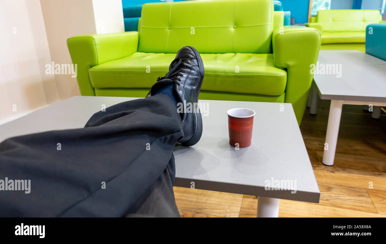 Man with his feet up on a table in dirty trainers having a cup of coffee Stock Photo
