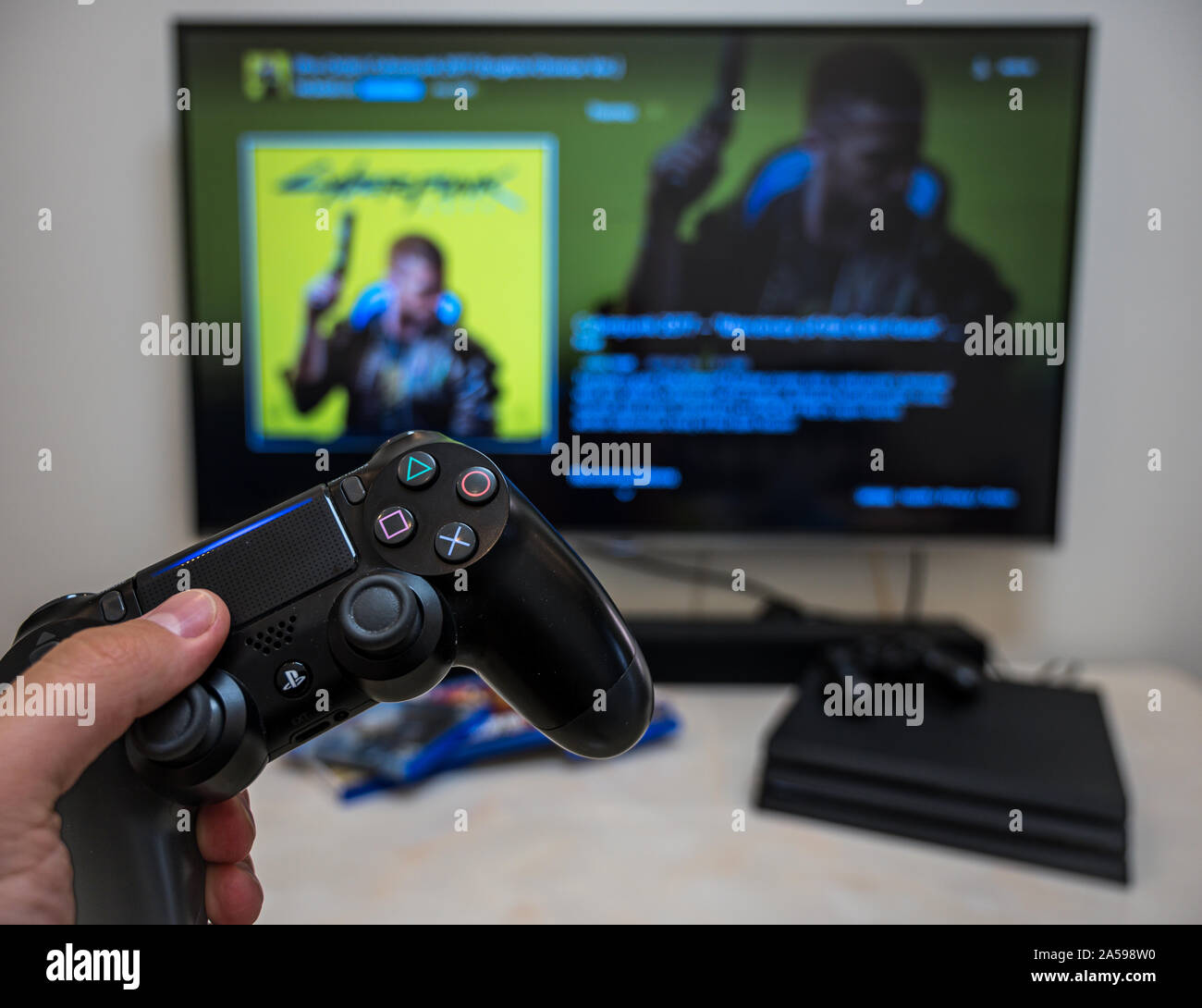 Pre-order, download, play Sony Play Station 4 Pro game Cyberpunk 2077 on the big LCD screen at home. Controller in the hand. Stock Photo