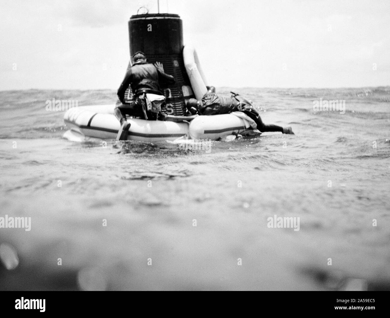 A U.S. Navy frogman team attaches a flotation collar to the Mercury-Atlas 9 (MA-9)Faith 7 spacecraft during recovery operations in the central Pacific near Midway Island. Stock Photo