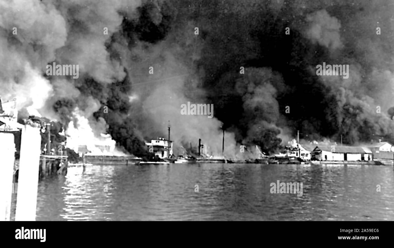 Fires at Cavite Navy Yard resulting from the Japanese air raid on December 10, 1941. Fifty-four bombers of the 11th Air Fleet were detailed from Formosa and attacked at 1300 hours. Twenty-seven attacked ships and small craft in the bay and the attack lasted for two hours. The entire yard was set ablaze; the power plant, dispensary, repair ships, warehouses, barracks, and radio station received direct hits. Greatest damage was done by the fire which spread rapidly and was soon out of control. Adm. Rockwell estimated that five hundred men were killed or seriously wounded. Stock Photo