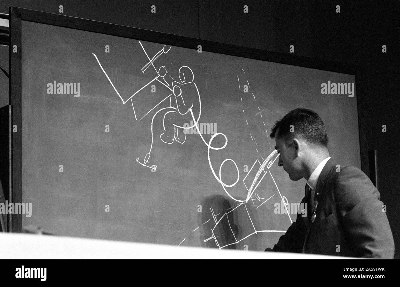 (1 Aug. 1966) --- Astronaut John W. Young, Gemini-10 command pilot, uses a chalk drawing on a blackboard to illustrate how astronaut Michael Collins, Gemini-10 pilot, looked when he inspected the Agena Target Docking Vehicle during his extravehicular activity. Stock Photo