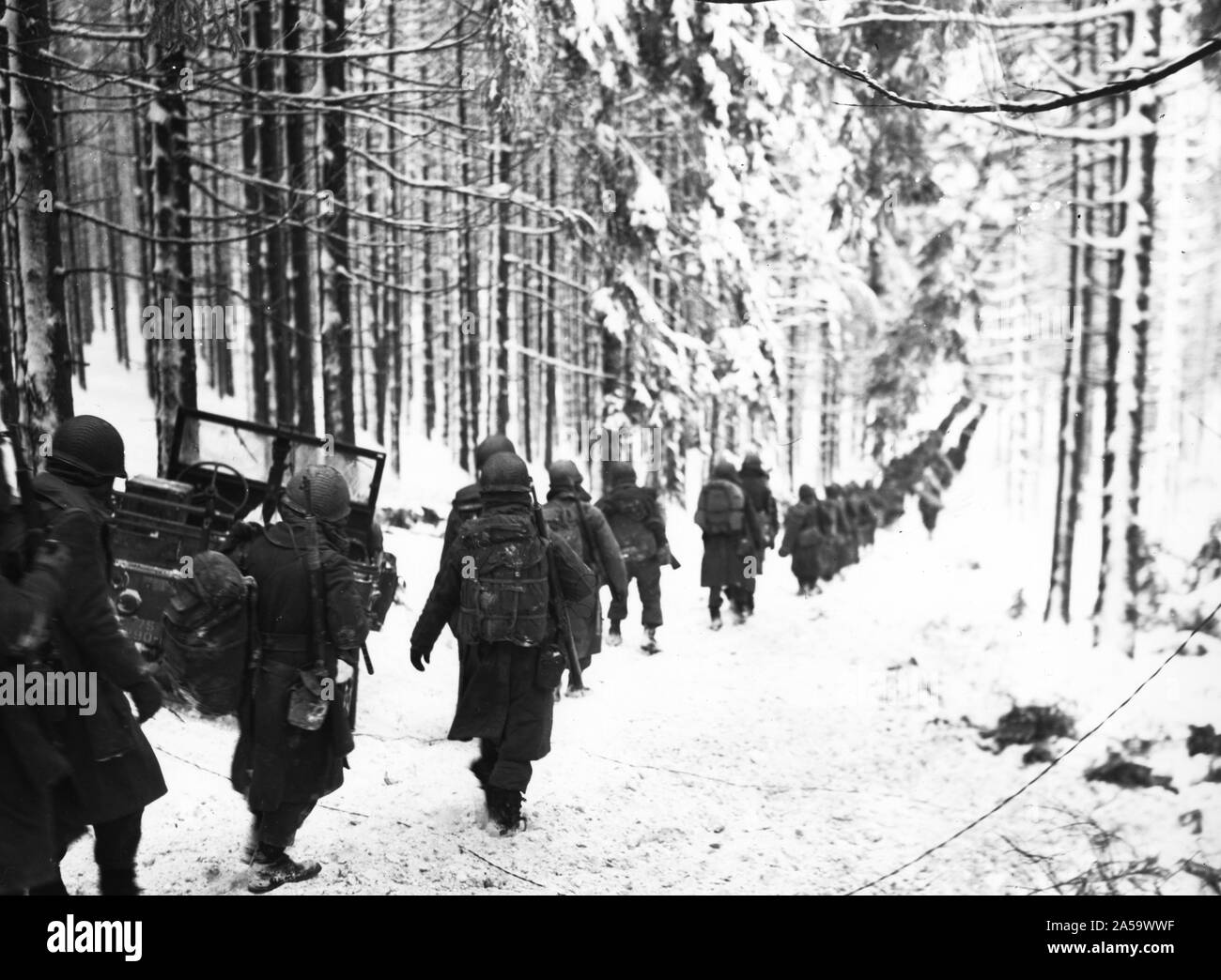 Original caption: American soldiers of the 75th Division march along the snow-covered road on the way to cut off the St. Vith-Houffalize road in Belgium. 1/24/45. Stock Photo