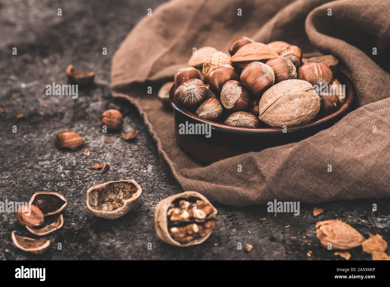 Nuts still life close-up. A small brown bowl with a selection of whole nuts - walnuts, hazelnuts, Brazil nuts and almonds. The nuts are on a dark ston Stock Photo
