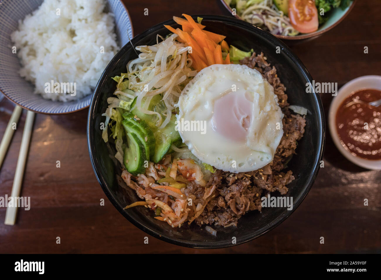 Organic korean Bi bim bap dish with rice, cucumber, beef,kochujang sauce, bean sprouts and carrots in a healthy meal on a table with other asian food Stock Photo