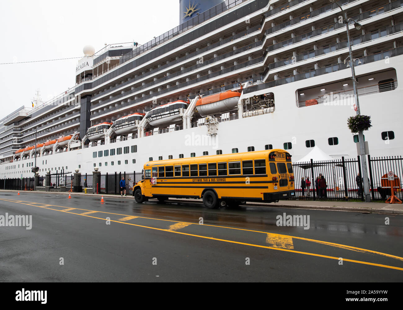 Yellow school bus parked alongside the cruise ship Arcadia in St John's Newfoundland, Canada Stock Photo