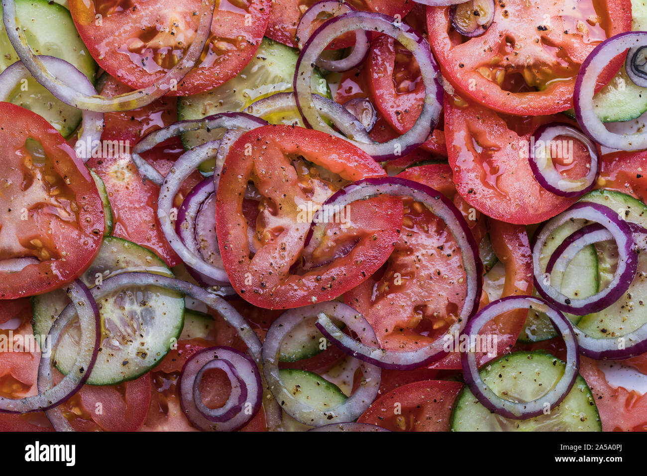 Close-up of a healthy organic salad with tomatoes, red onion and cucumber, seen from above. There are crushed black peppercorns and olive oil on the s Stock Photo