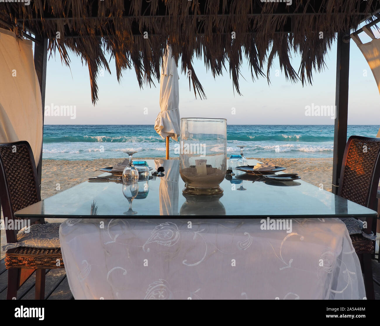 Gazebo on the beach with table set. Candle on table. Relaxing context. Nobody on the beach. Blue sea on the back. Fabulous holiday Stock Photo