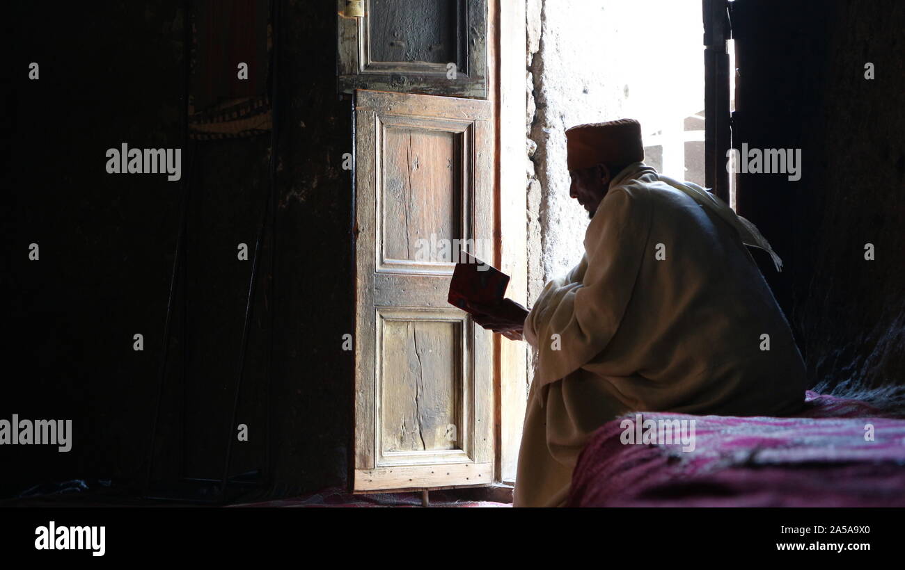 Lalibela/Ethiopia - April 20, 2019: Orthodox monk reads the bible by door light in Asheton Maryam Monastery Stock Photo