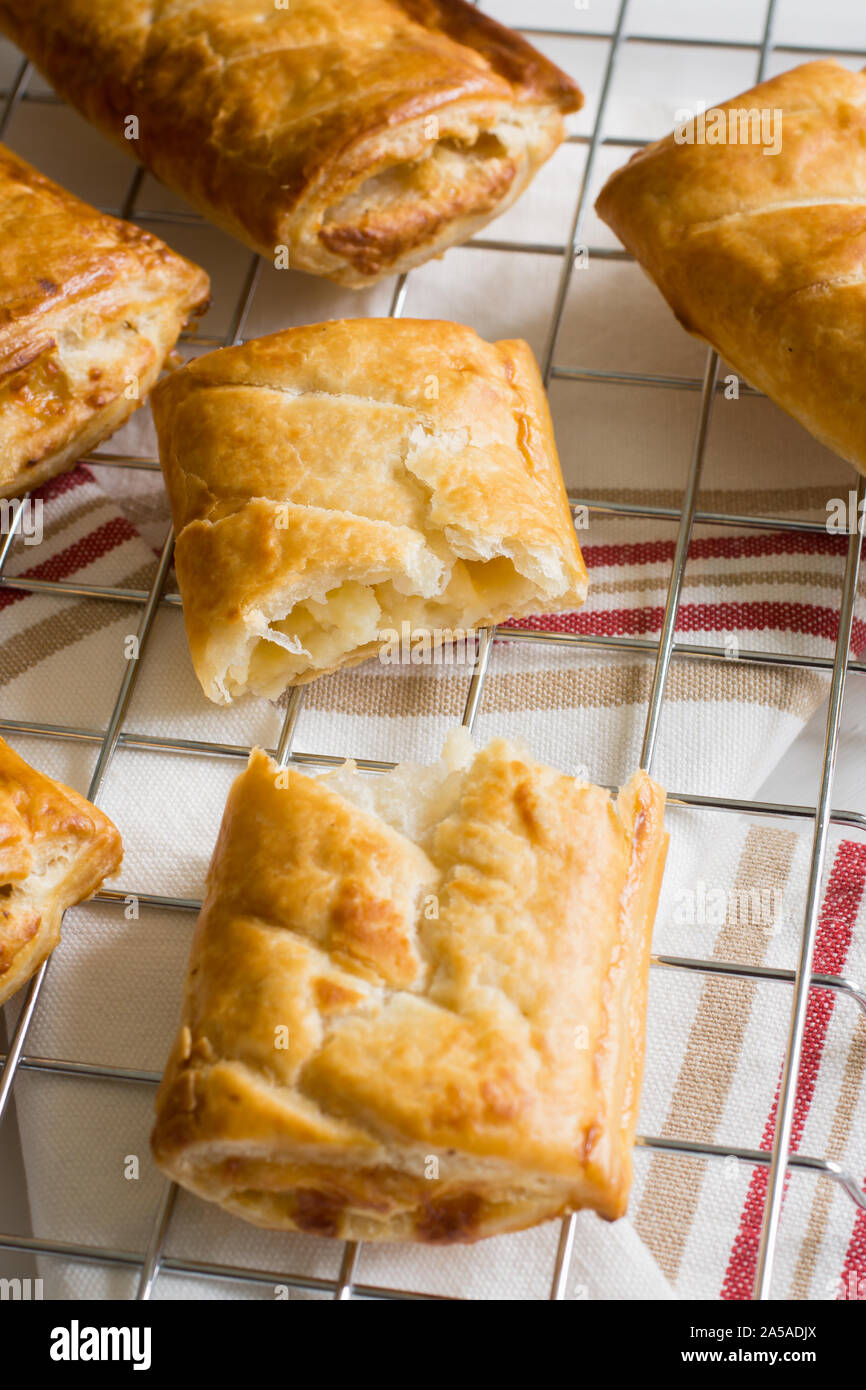 Savory cheese and onion puff pastry rolls fresh out of the oven cooling on a cooking trivet a vegetarian alternative to the usual sausage roll Stock Photo