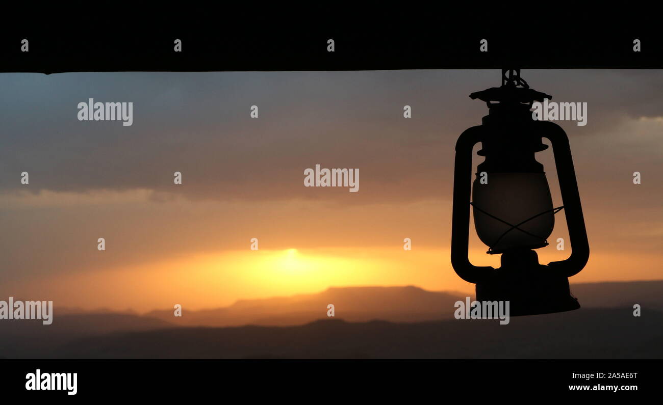 Paraffin oil lantern hanging from a beam silhouetted against a setting sun Stock Photo
