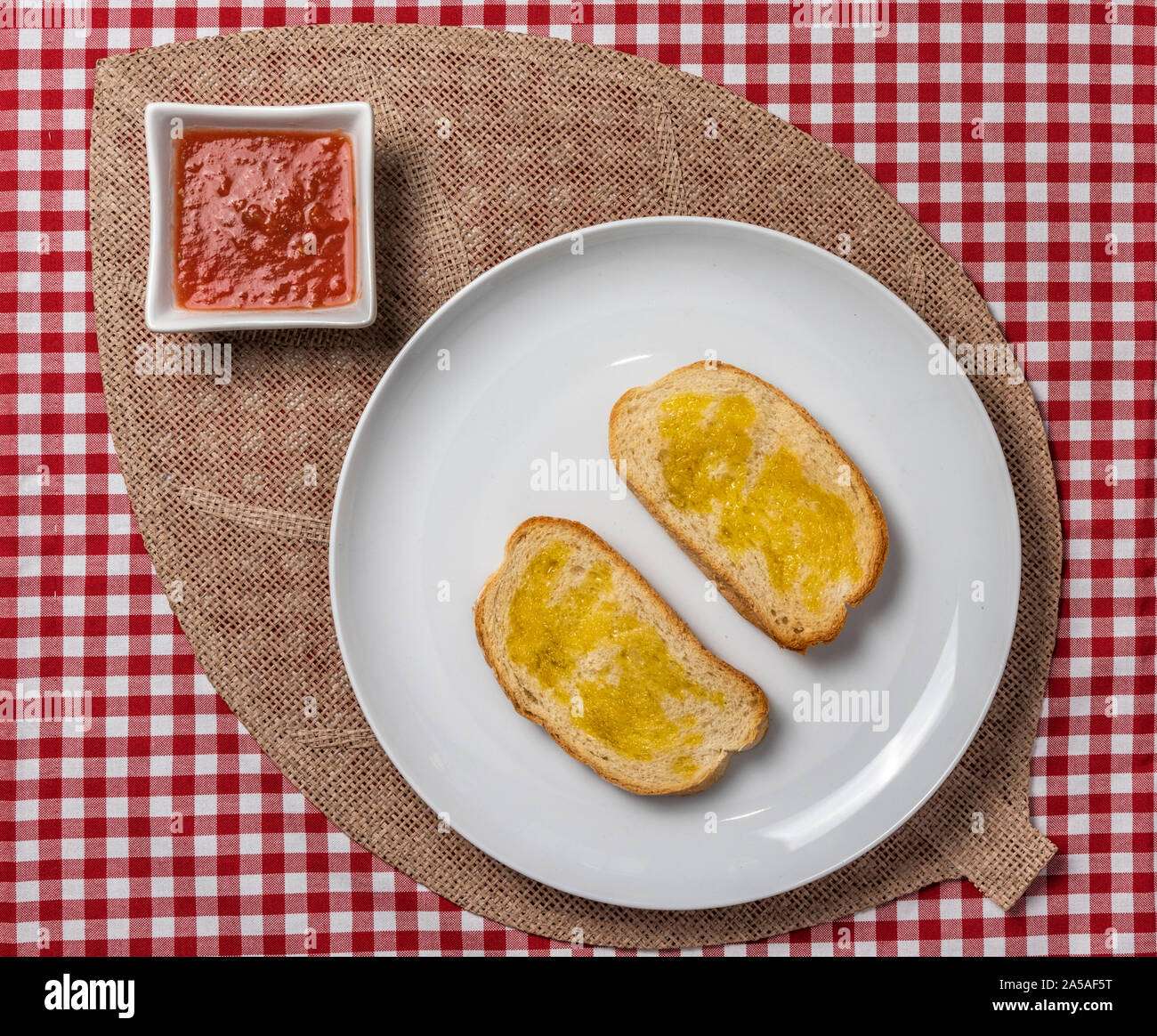 Delicious Mediterranean breakfast consisting of toast with oil and tomato and a coffee, served on a vintage checked tablecloth and a burlap napkin. Ho Stock Photo