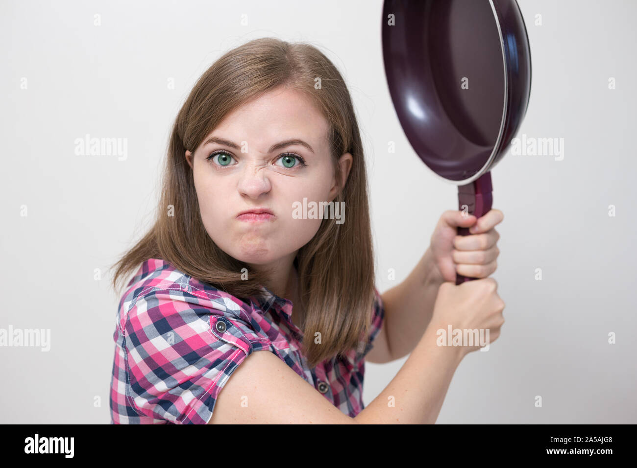 Young caucasian girl woman threaten to hit with frying pan. Angry, defensive or aggressive Stock Photo