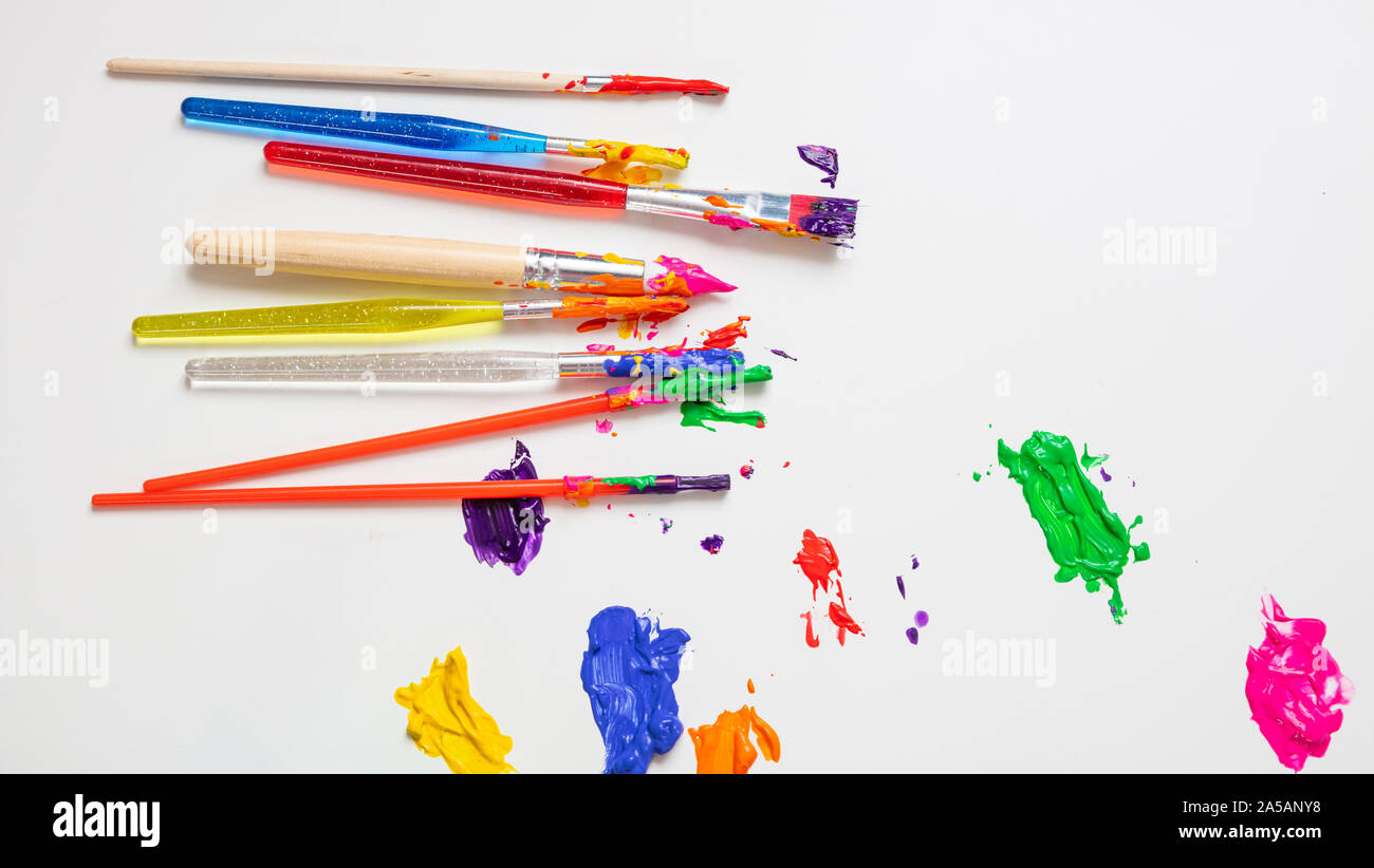 Kids creativity. Colorful finger paints and paint brushes on white color background, top view, copy space Stock Photo