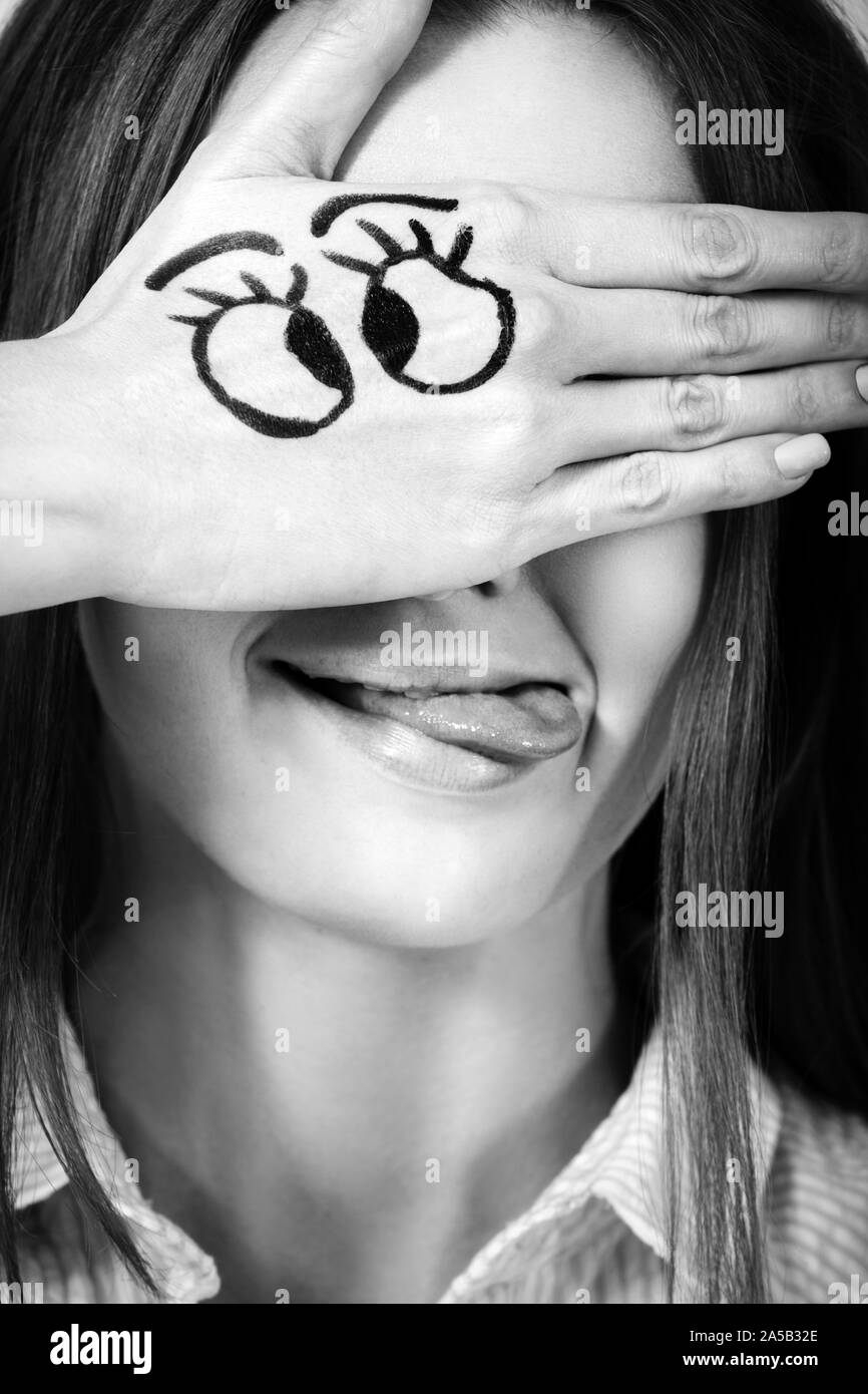 fun girl with drawn eyes on palm cover her face, show tongue smiling, monochrome Stock Photo