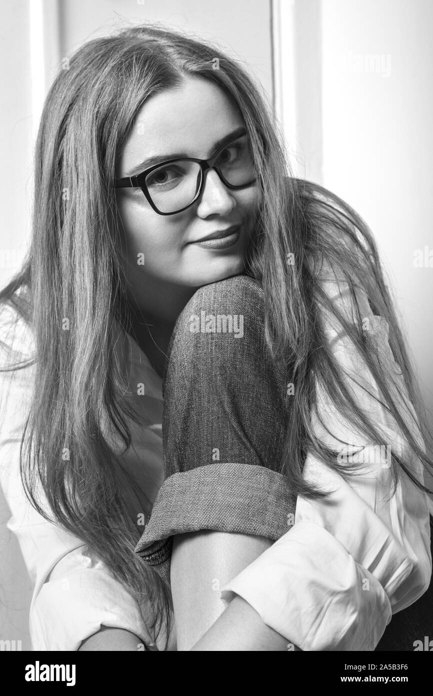 happy young blond woman in eyeglasses sitting smiling looking at camera, monochrome Stock Photo