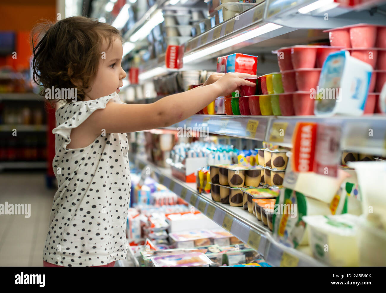 Little girl buying yogurt in supermarket. Child in supermarket select products from store showcase. Concept for children selecting milk products in sh Stock Photo