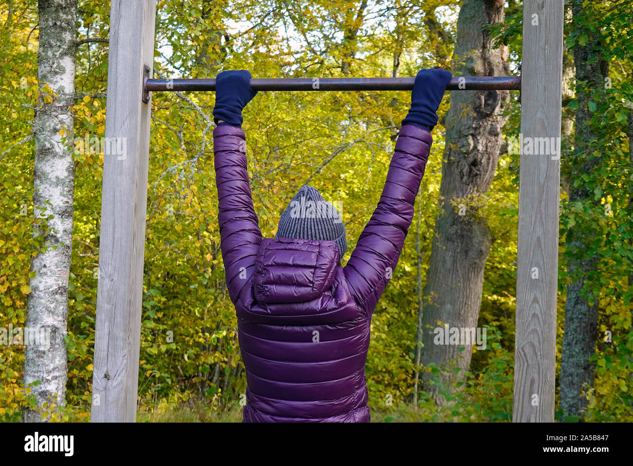 Woman doing pull ups outdoor in park. Middle aged female enjoying beautiful autumn day, and increase her welfare by outdoor activities. Stock Photo