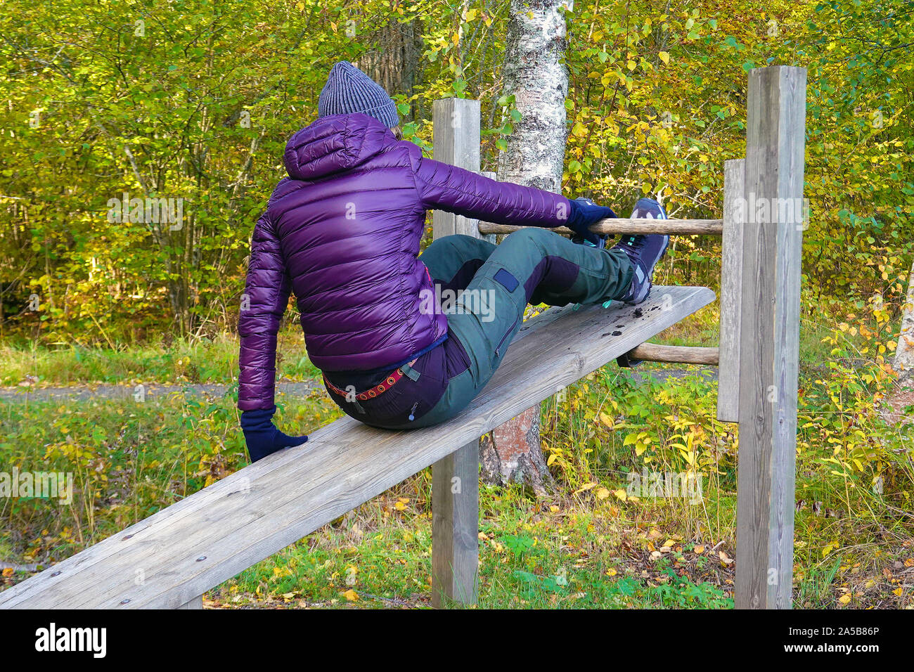 Woman start doing sit ups outdoor in park. Middle aged female enjoying beautiful autumn day, and increase her welfare by outdoor activities. Stock Photo