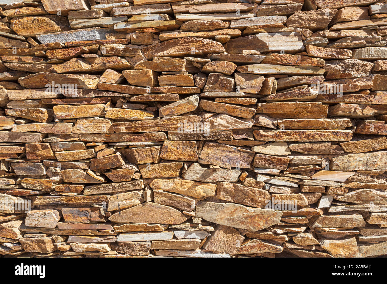 wall of yellow colored slate stones that are expertly stacked without cement Stock Photo