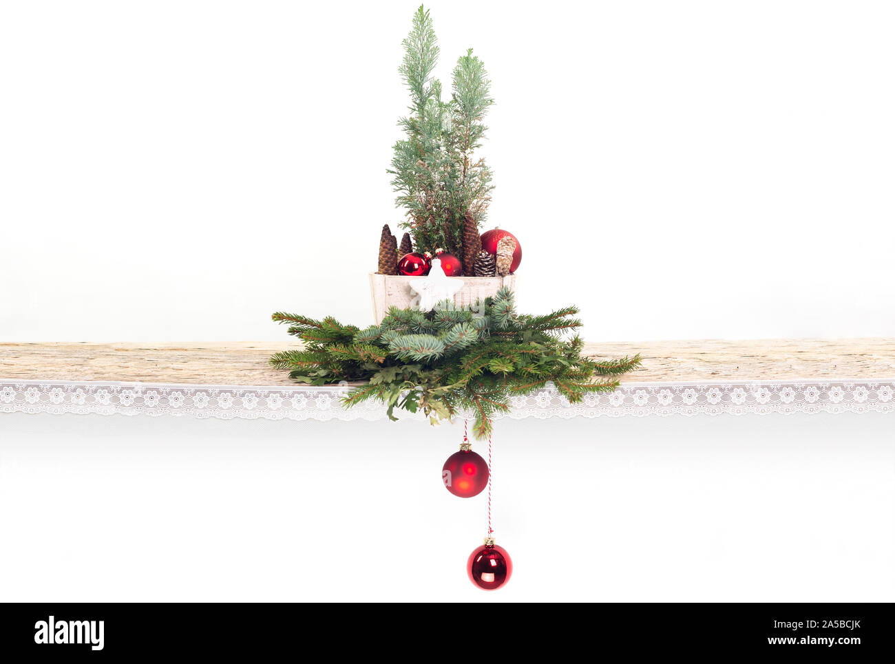 An old wooden board decorated with lace. Fir branches red and blue. A wooden box with conifer, pine cones and balls. 2 red Christmas balls are hanging Stock Photo