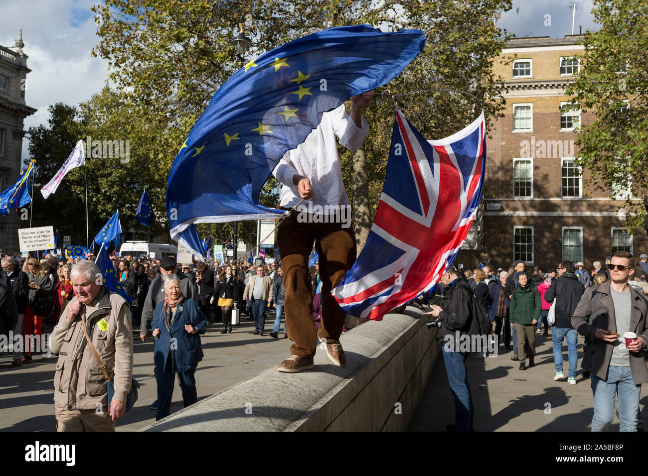 On the day that Members of Parliament sat on a Saturday (the first time in 37 years and dubbed 'Super Saturday') in order to vote for Prime Minister Boris Johnson's Brexit deal with the EU in Brussels, a young man waves an EU and Union Jack flags alongside a million Remainers (according to organisers) who marched through the capital to voice their opposition to a Brexit and calling for a peoples' Vote, on 19th October 2019, in London, England. Stock Photo