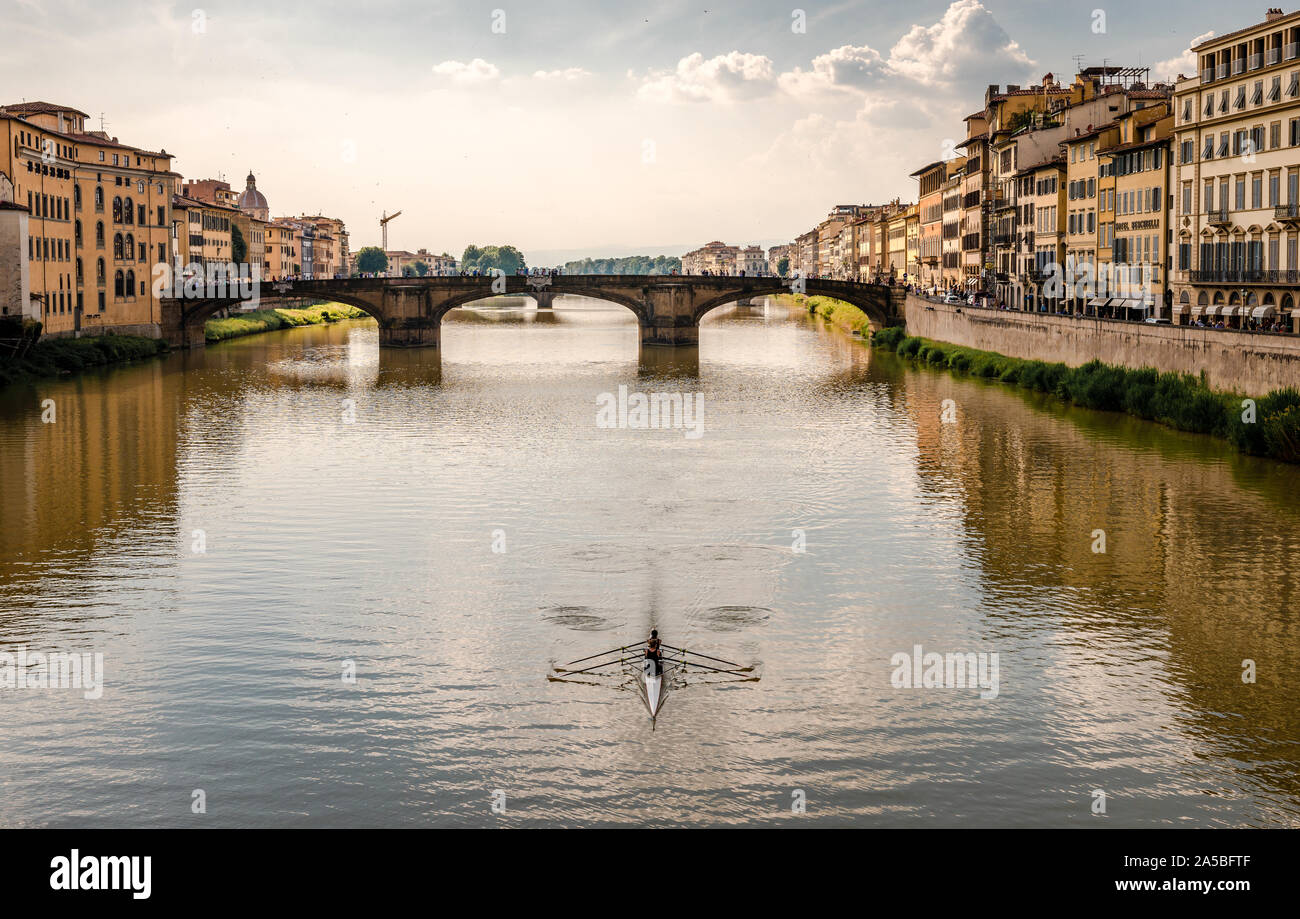 Florence, Italy: A rowing boat in river Arno, with old medieval buildings in the riverbanks and St. Trinity Bridge in the background. Stock Photo
