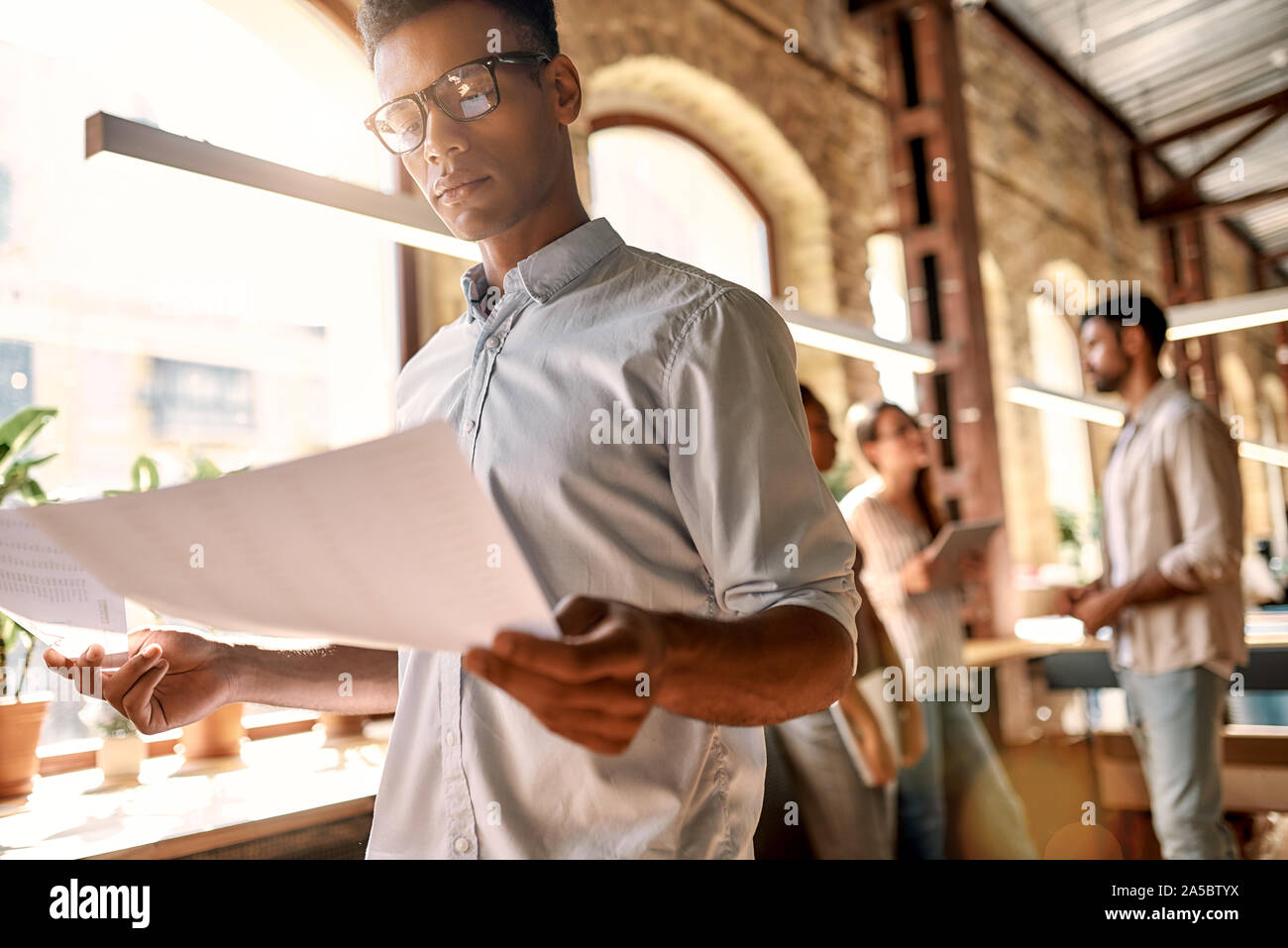 Working on new project. Young afro american man in casual clothes analyzing documents while standing in the modern office Stock Photo