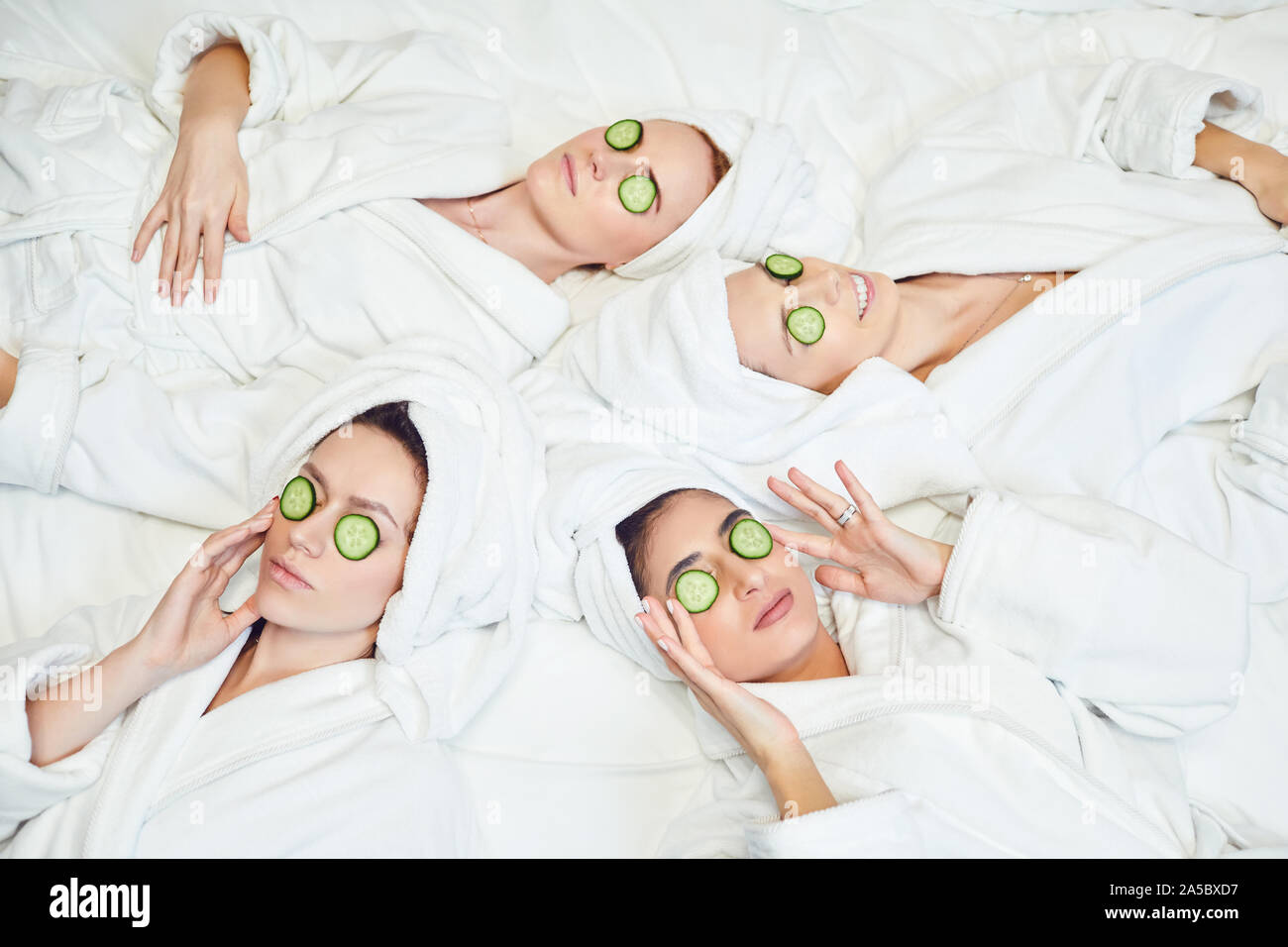 Chilling women in bathrobes with cucumber slices on face Stock Photo