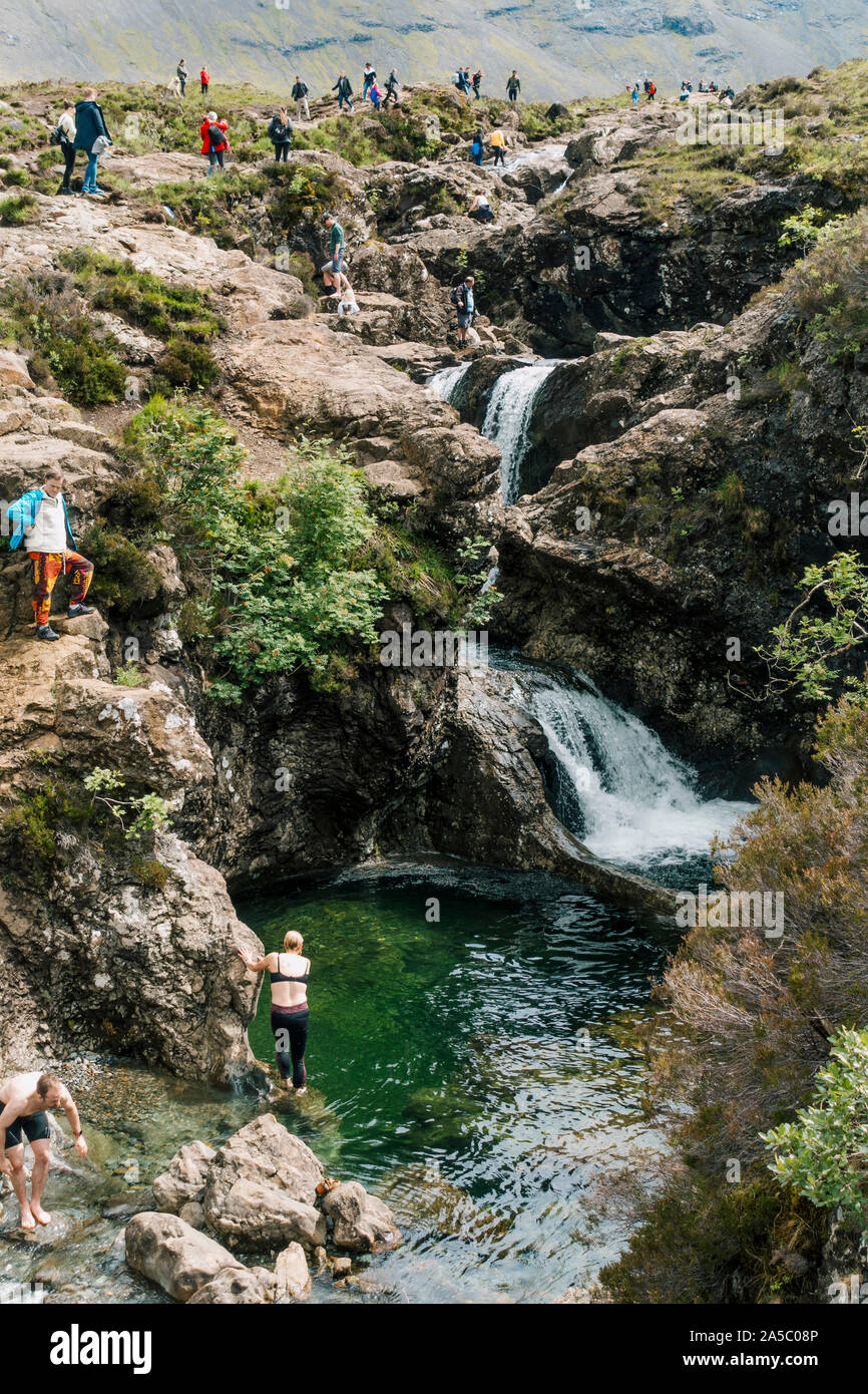 Tourists swim and clamber over waterfalls and rocks at the Fairy Pools, a famous tourist attraction on the Isle of Skye, Scotland Stock Photo
