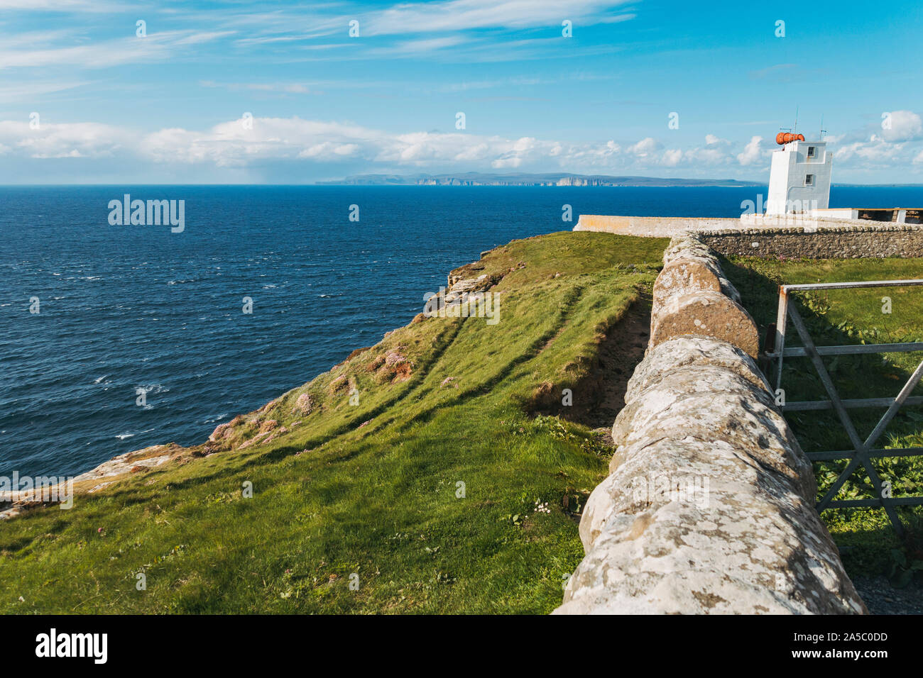 Sea crashes onto the cliffs by the Dunnet Head Lighthouse perimeter on a sunny spring afternoon, at the northernmost point on British mainland Stock Photo