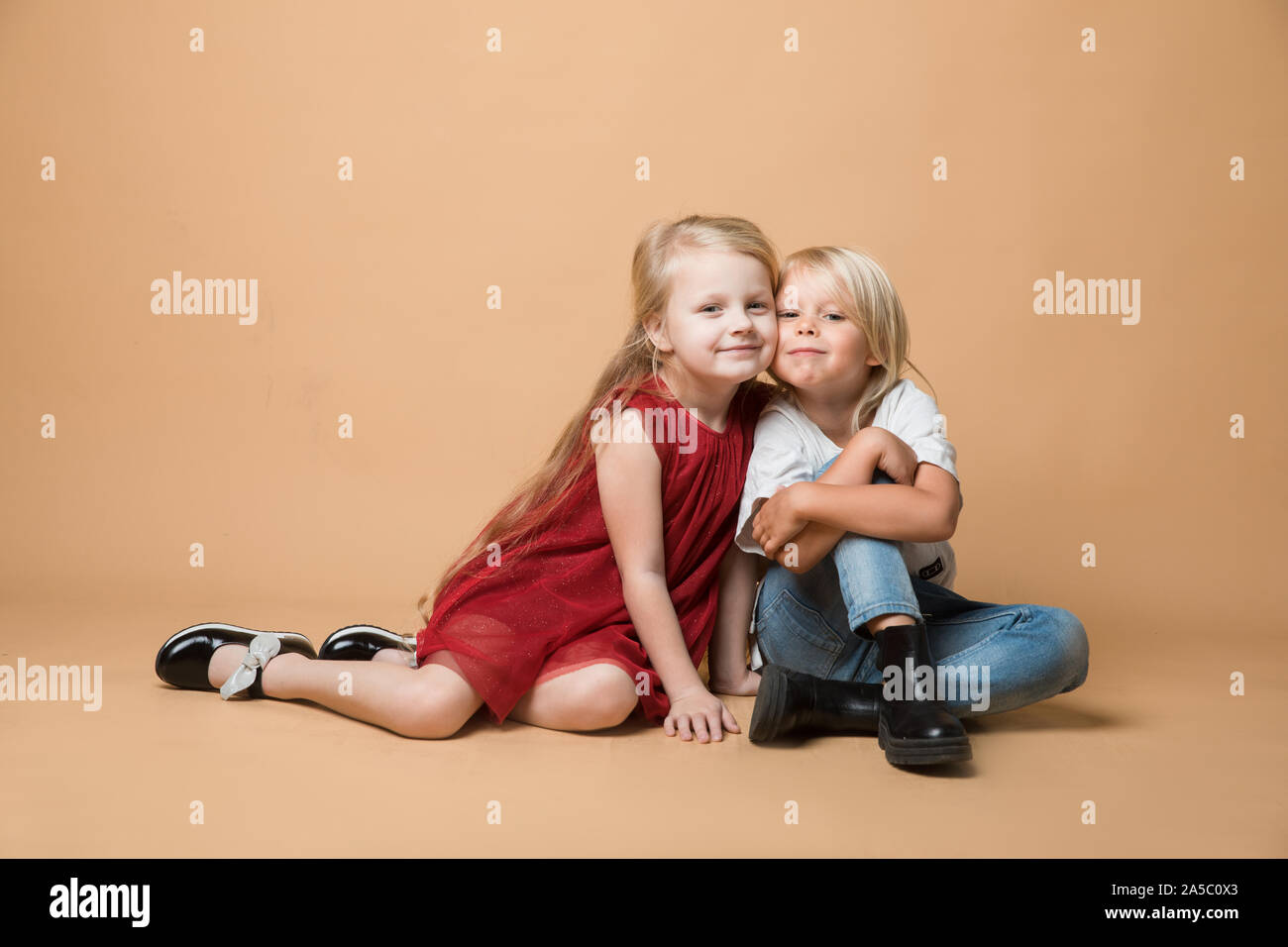A boy and a girl sit on the floor on an orange background. The children ...