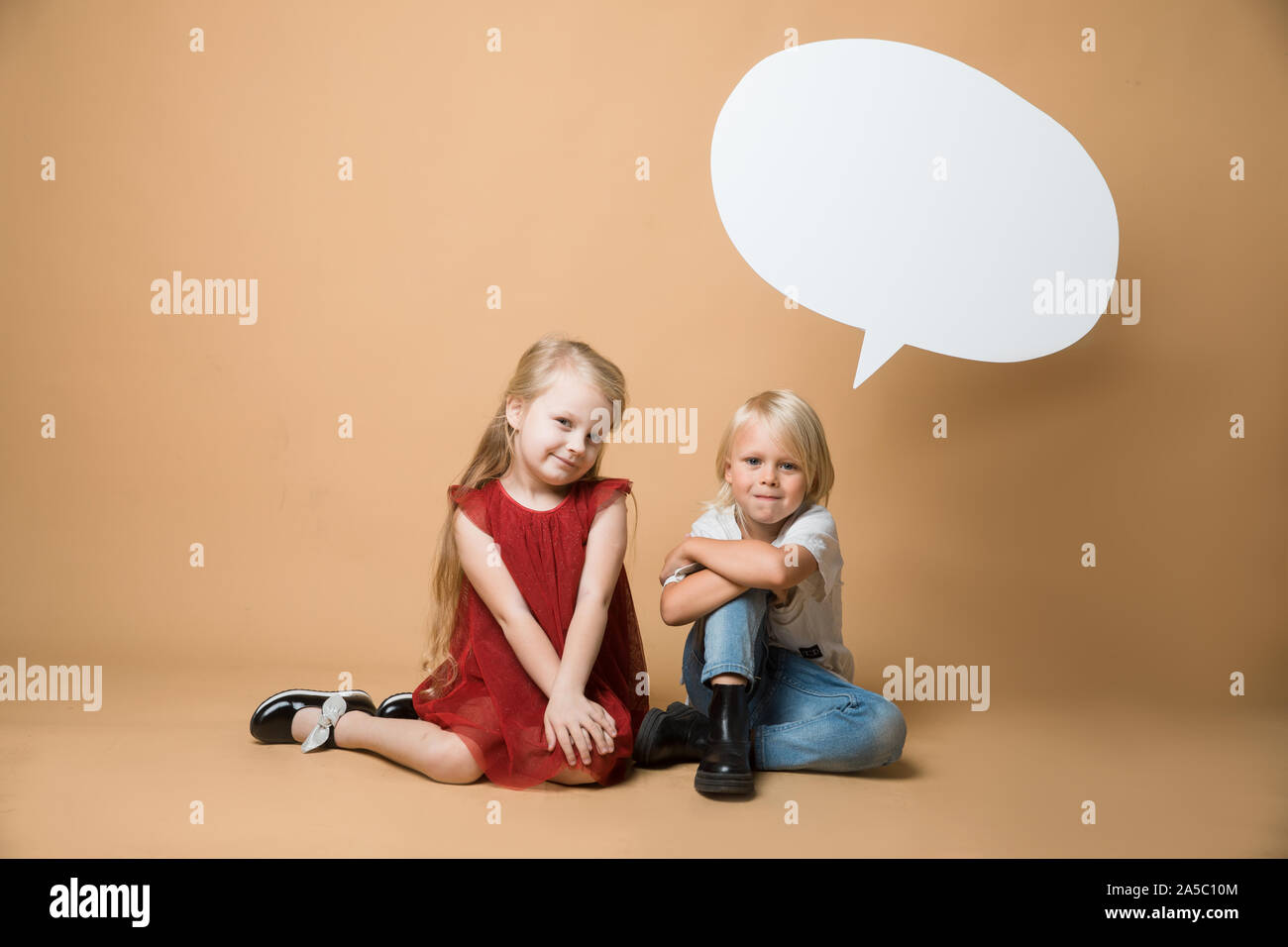 A boy and a girl sit on the floor on an orange background. The children ...