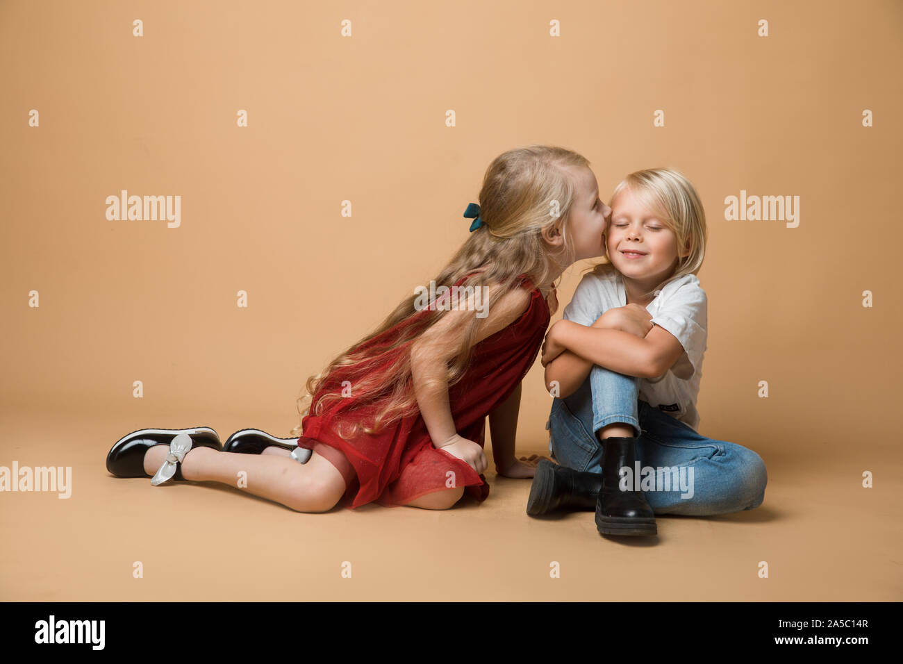 A boy and a girl sit on the floor on an orange background. The children ...